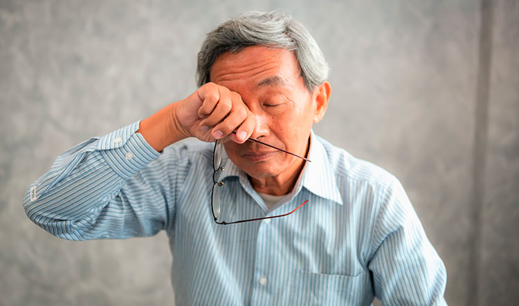 Eye Doctors Near Me - Older man holding his eyeglasses while wiping closed dry eyes.